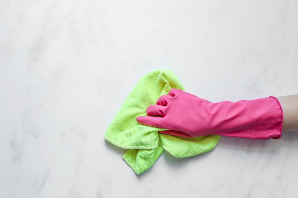 A person using pink rubber glove and green cleaning cloth